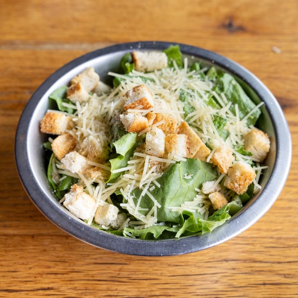 Caesar salad with green lettuce, croutons, and shredded Parmesan cheese in a metal bowl.