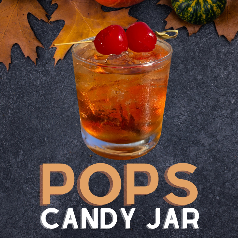 Amber cocktail in a rocks glass garnished with two red cherries, autumn leaves, and gourds, labeled “Pops Candy Jar.”