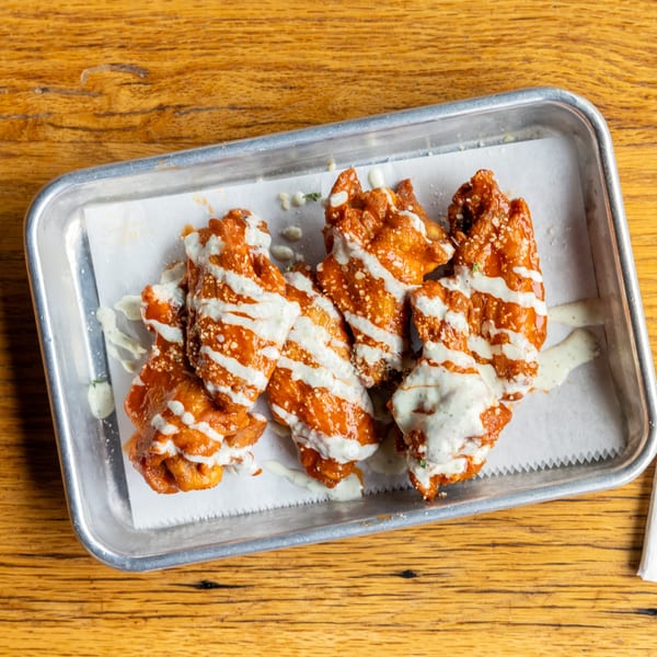 Felix's Pizza Pub's buffalo wings, drizzled with ranch dressing and parmesan cheese, on a metal tray.
