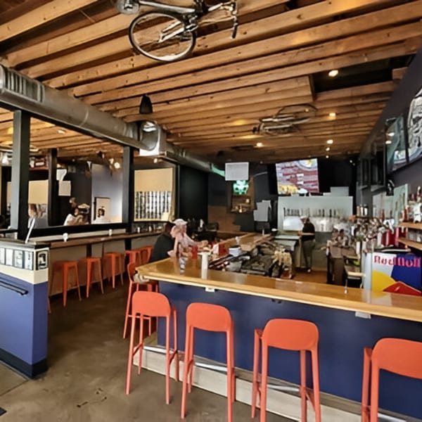Interior of Felix's Pizza Pub with a long bar, orange stools, and exposed wooden beams.