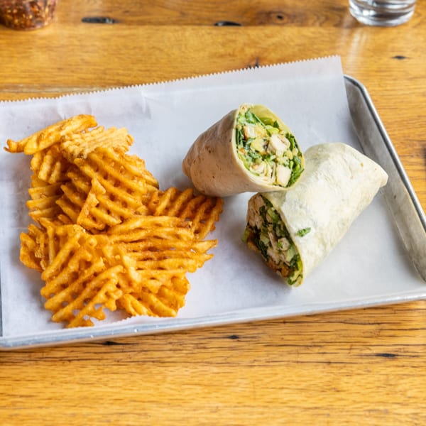 Two chicken wraps with waffle fries on a metal tray with white parchment paper.