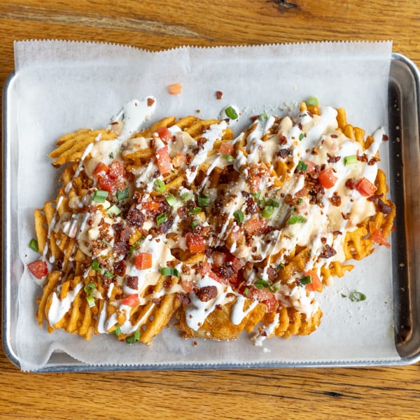 Loaded waffle fries from Felix's Pizza Pub, topped with cheese sauce, bacon, tomatoes, and green onions.