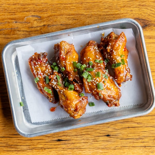 Felix's Pizza Pub's sweet chili wings, garnished with sesame seeds and green onions, on a metal tray.