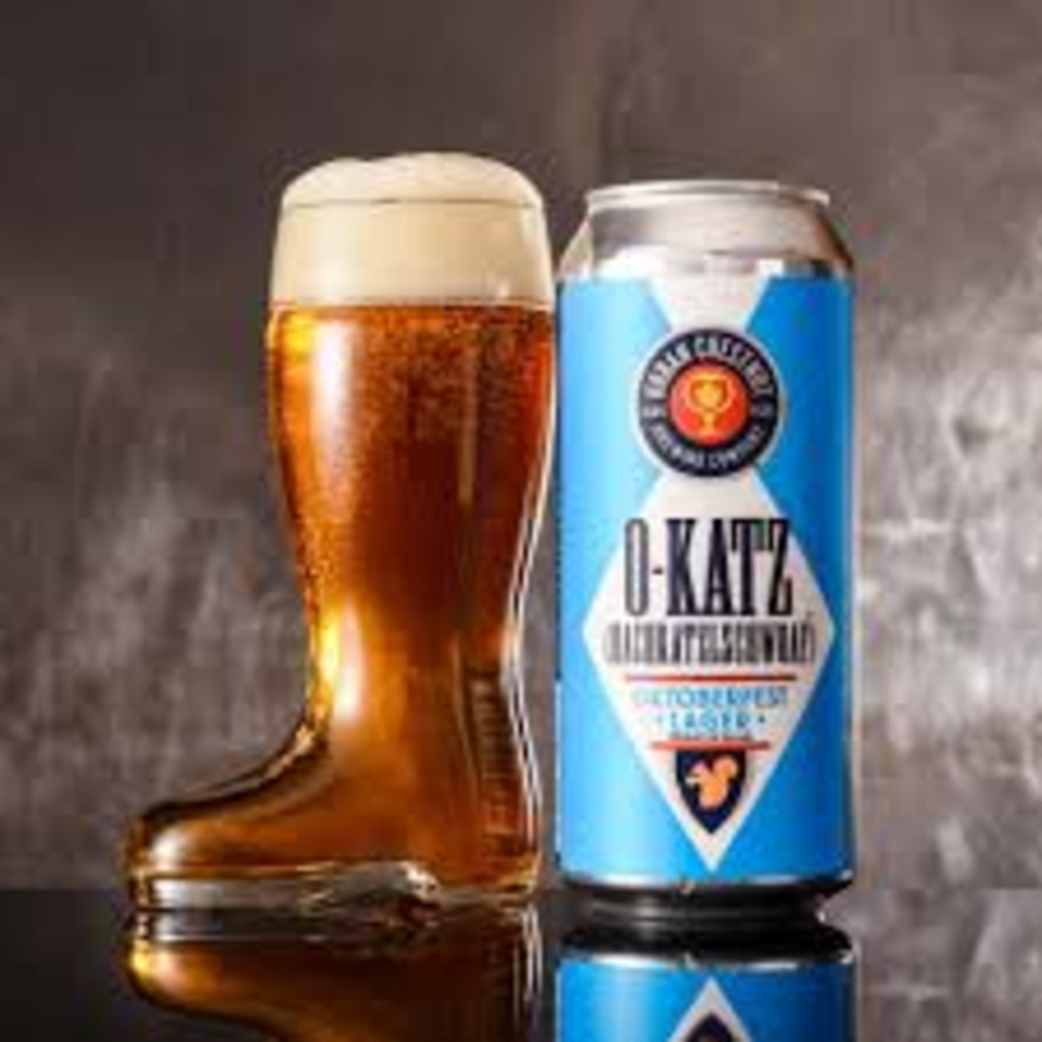 Foamy amber beer in a glass beside a blue-and-white O-Katz Czech craft beer can on a reflective surface.